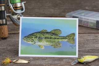 Card with a large mouth bass illustration on a wooden surface with fishing equipment.