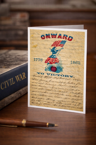 Vintage-style card with patriotic design featuring a flag and text, placed on a wooden surface with a pen and book in the background.