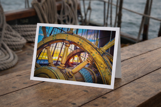 Greeting card with ship wheel design on wooden surface near water