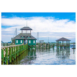 Dock with green buildings and wooden walkway over water under a blue sky.