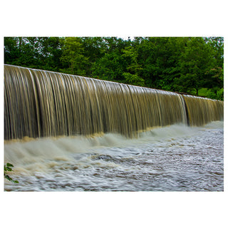 Starr Mill Waterfall with a smooth curtain of cascading water flowing over a low dam, surrounded by lush green trees and a fast-moving river below.