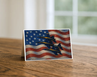 Blue Angels diamond formation American flag 5x7 greeting card from Will Davis Studios displayed standing on a wooden table near a bright window — four US Navy F/A-18 Hornets in diamond formation against painterly American flag, naval aviation patriotic fine art card