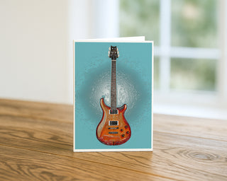 Modern electric guitar art greeting card displayed upright on a wooden table with soft window light background, 5x7 music-themed greeting card design