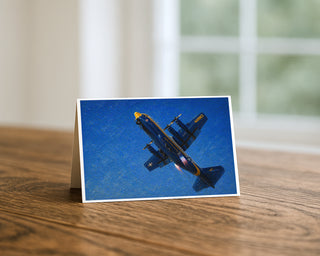 Albert C-130 oil painting 5x7 greeting card from Will Davis Studios displayed standing on a wooden table near a bright window — US Marine Corps C-130 Hercules in Blue Angels blue and gold colors during powered climb, Marine aviation fine art card