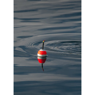 Fine art photograph of a classic red and white fishing bobber floating on a calm blue-gray water surface with a perfect reflection below and gentle concentric ripples spreading outward, with a thin fishing line tracing across the surface, printed as a 5x7 greeting card by Will Davis Studios.