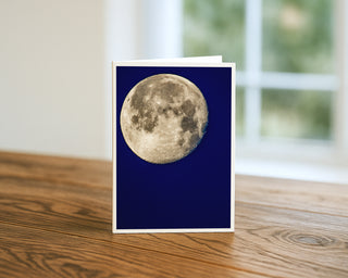 5x7 greeting card featuring a detailed full moon against a deep blue night sky, fine art photography by Matt Punches displayed on a tabletop.