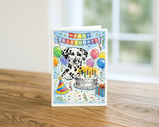 Happy Birthday Dalmatian dog greeting card displayed on a wooden table with colorful balloons, confetti, party hat, and birthday cake, fun 5x7 birthday card by Will Davis Studios