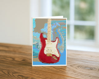 Red electric guitar fine art greeting card standing on a wooden table, colorful music-themed 5x7 card design by Will Davis Studios.