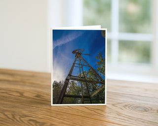 Rustic farm windmill viewed from below against a deep blue sky and trees, landscape photography greeting card by Will Davis Studios.