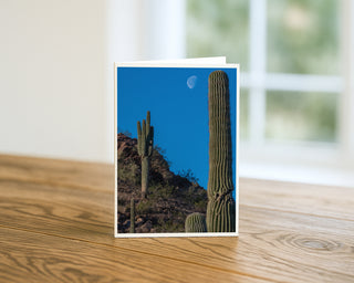 Photograph of saguaro cacti on a desert hillside with the moon in a clear blue sky, Arizona landscape greeting card by Will Davis Studios