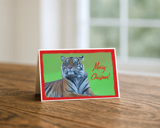 Tiger Merry Christmas fine art wildlife photography greeting card displayed on a wooden table, featuring a majestic tiger with festive red border and holiday message, 5x7 Christmas card by Matt Punches from Will Davis Studios.