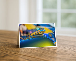 Will Davis Studios Vintage chrome hood ornament on a classic automobile photographed in bright colors, displayed on a 5x7 greeting card on a wooden table