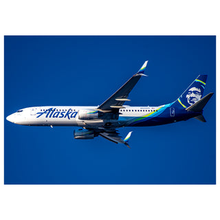 Alaska Airlines airplane flying against a clear blue sky Will Davis Studios