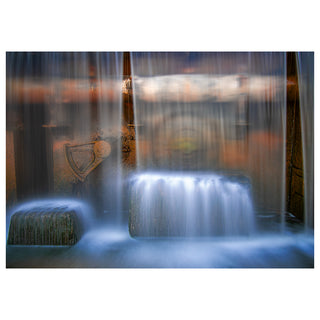 Fine art greeting card featuring a breathtaking long exposure photograph of Arizona Falls on the Phoenix Arizona Canal, shot from behind the waterfall looking out through silken curtains of blue-white water descending in perfect parallel lines, revealing warm amber and rust-toned historic cast iron gate hardware, weathered metal machinery, and mossy stone structures beyond the shimmering veil of falling water, the cool blue tones of the cascading water contrasting dramatically with the rich warm textures of