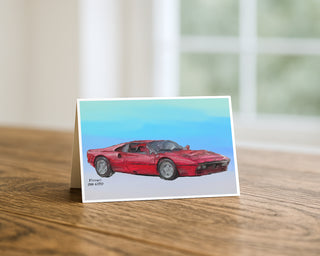Will Davis Studios 5x7 greeting card featuring an illustration of a red Ferrari 288 GTO sports car on a soft blue gradient background, displayed standing on a wooden table with a white envelope.
