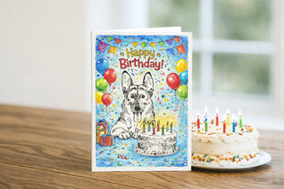 Birthday card with a dog and cake illustration next to a small cake with candles on a wooden table. German Shepherd. Will Davis Studios