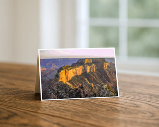 Greeting card with a scenic landscape of cliffs and mountains on a wooden surface.