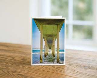 Greeting card with a scenic view of a pier on a wooden surface by Will Davis Studios