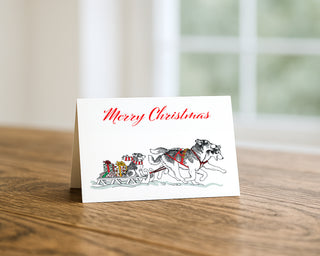 Merry Christmas card with Siberian Huskies pulling a sled illustration on a wooden surface