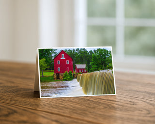 Greeting card with a red barn and waterfall on a wooden surface Will Davis Studios